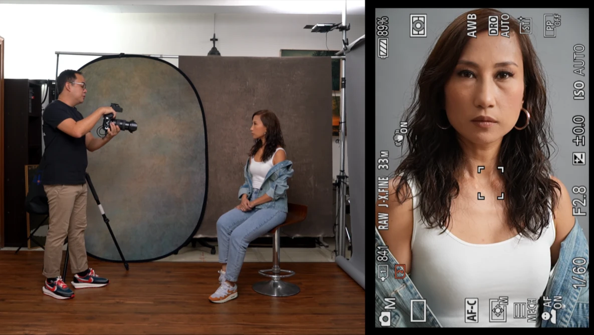 Portrait monitor display showing a woman's headshot while a photographer adjusts a large circular reflector during a studio portrait session.