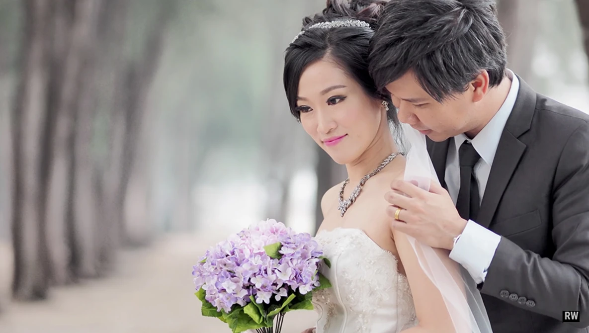 Bride and groom posing together with purple hydrangea bouquet in soft-focus outdoor setting.