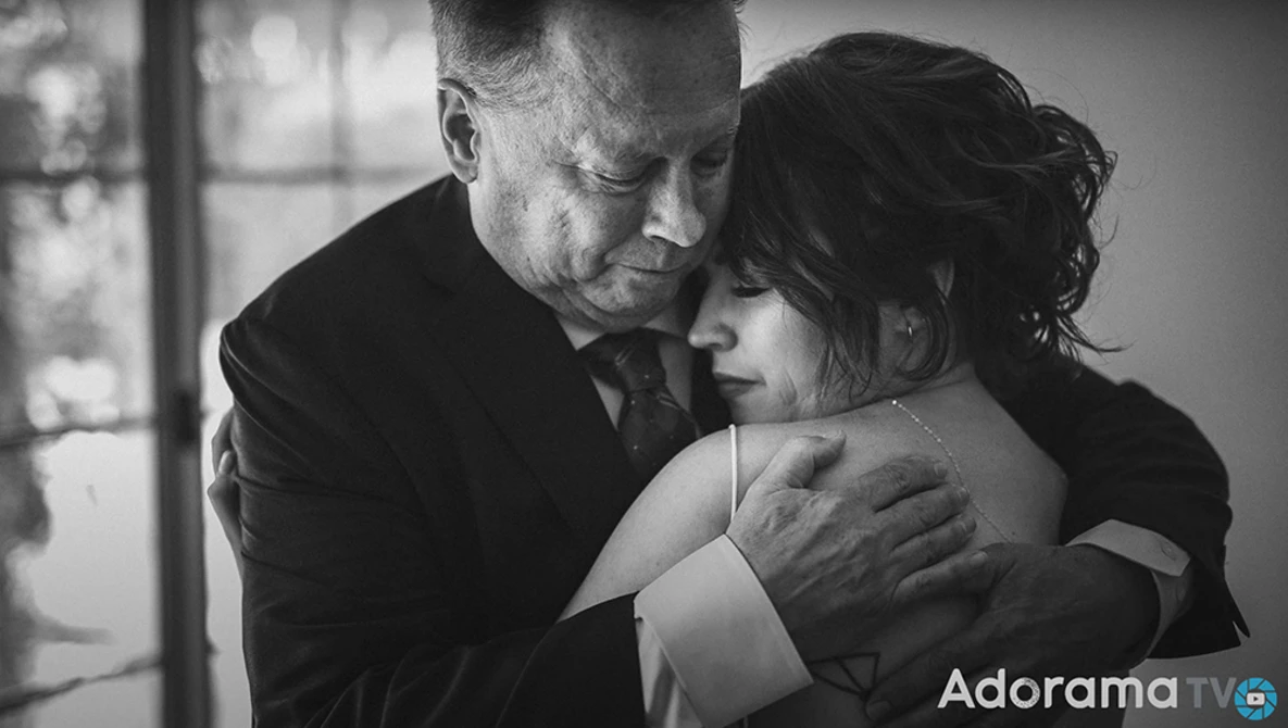 Man in dark suit embracing woman from behind in black and white portrait.