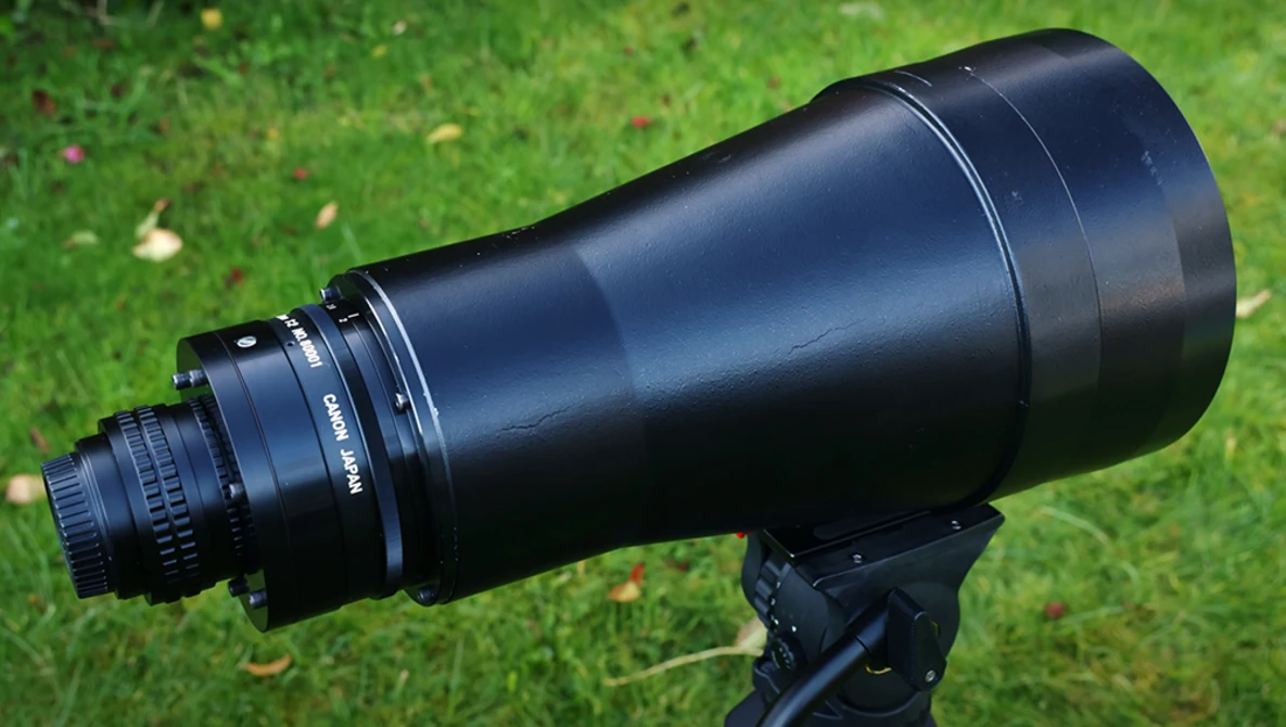Black telephoto lens mounted on a tripod against a grass background.