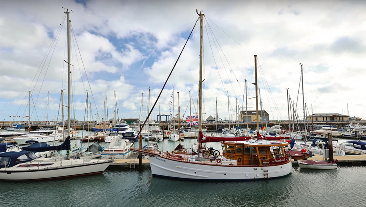 Marina filled with sailboats moored at docks under partly cloudy sky.
