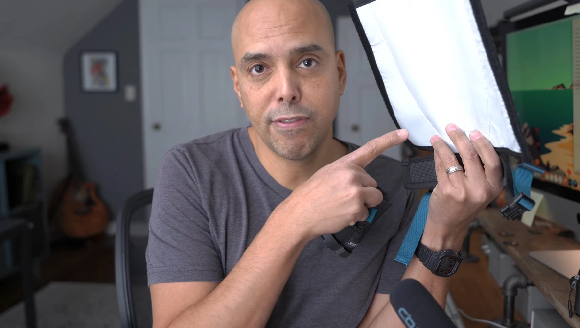 Man in a gray t-shirt demonstrating a photography lighting modifier with a white diffusion panel.