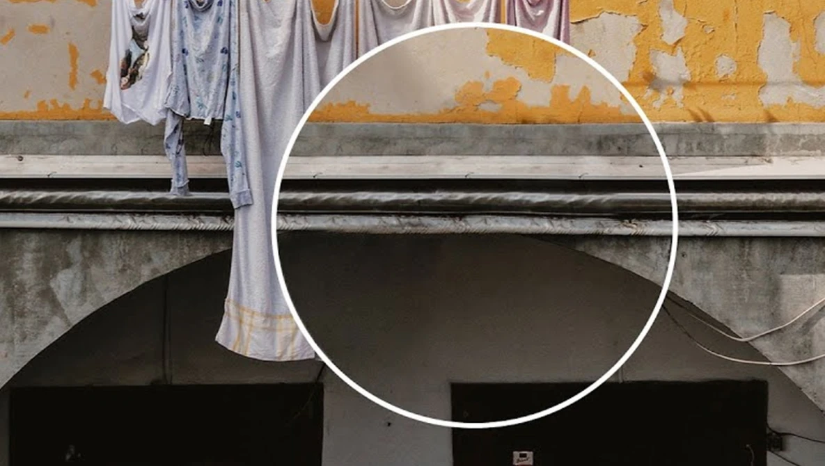 Weathered yellow and gray building facade with white circle overlay and hanging laundry on upper level.