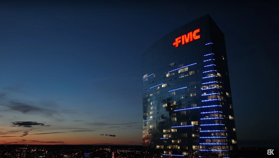 Illuminated office tower at dusk with red FMC sign glowing against twilight sky.
