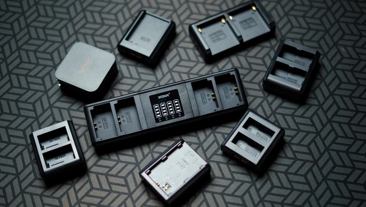 Collection of camera battery chargers and batteries arranged on a patterned surface.
