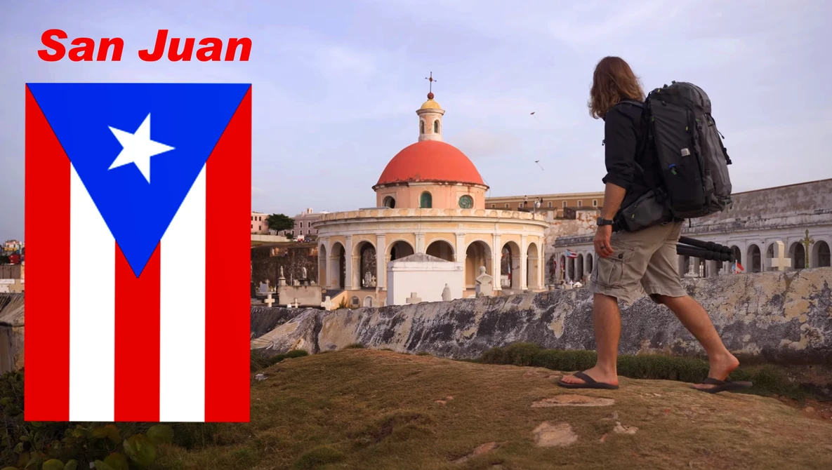Traveler with backpack standing on rocky terrain overlooking a colonial dome building with Puerto Rican flag displayed on left.
