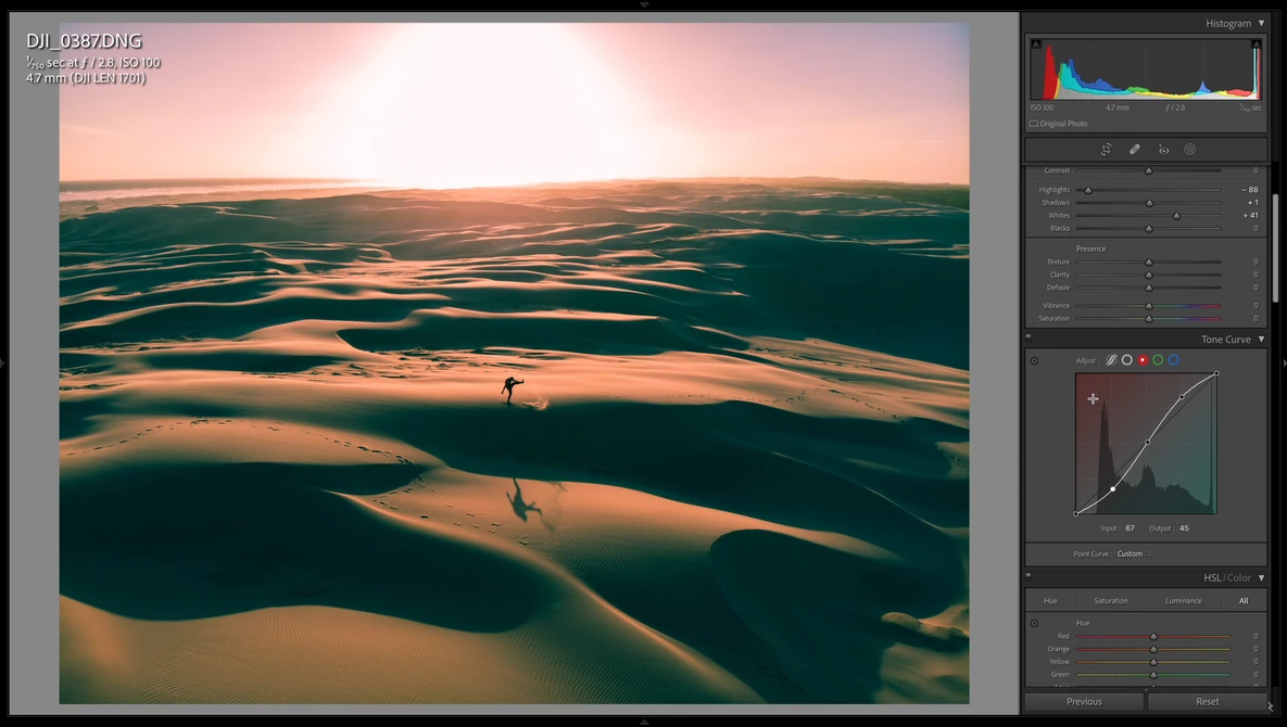 Aerial view of sand dunes with two figures walking across the rippled landscape at golden hour.