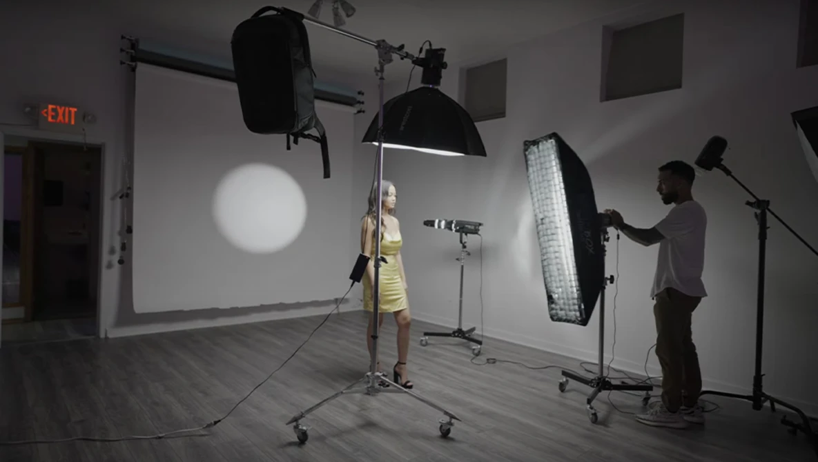 Professional photo shoot setup with model in yellow dress and lighting crew adjusting equipment.