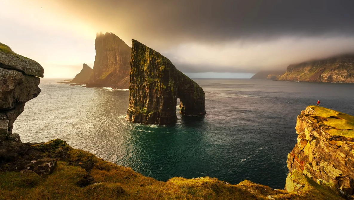 Dramatic coastal landscape with tall sea stacks rising from ocean and moss-covered cliffs bathed in golden light.