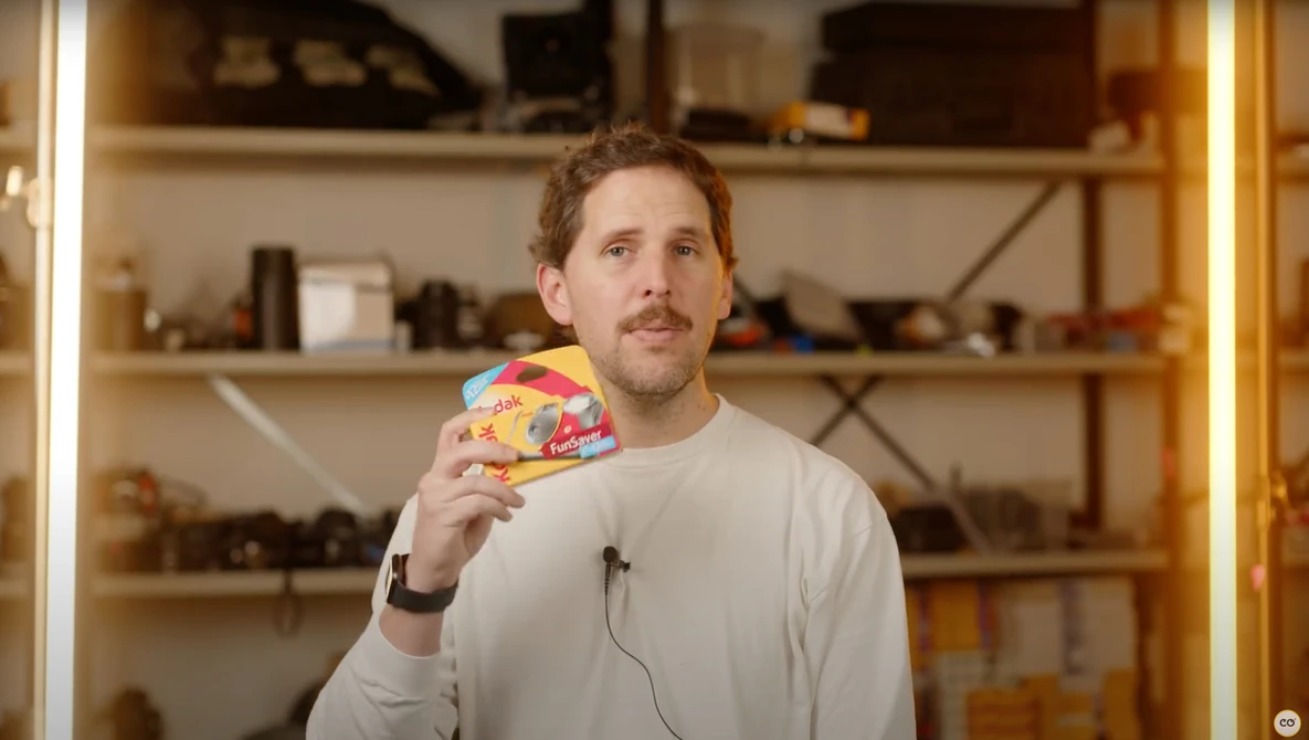 Man holding a colorful patterned object while looking upward in a studio setting with wooden shelving.