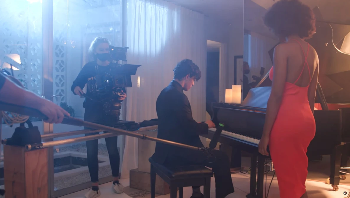 Cinematographer operating a camera while woman in red dress stands nearby during what appears to be a film or television production shoot.