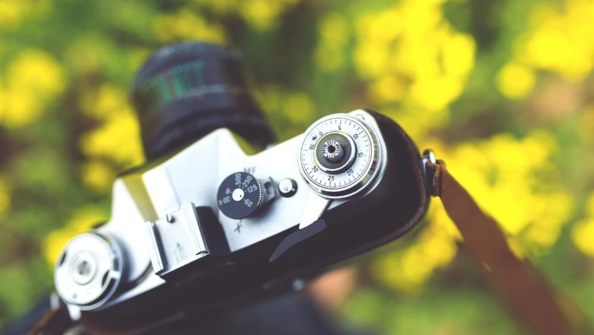 Vintage rangefinder camera with chrome lens and black body displayed against blurred yellow-green foliage background.
