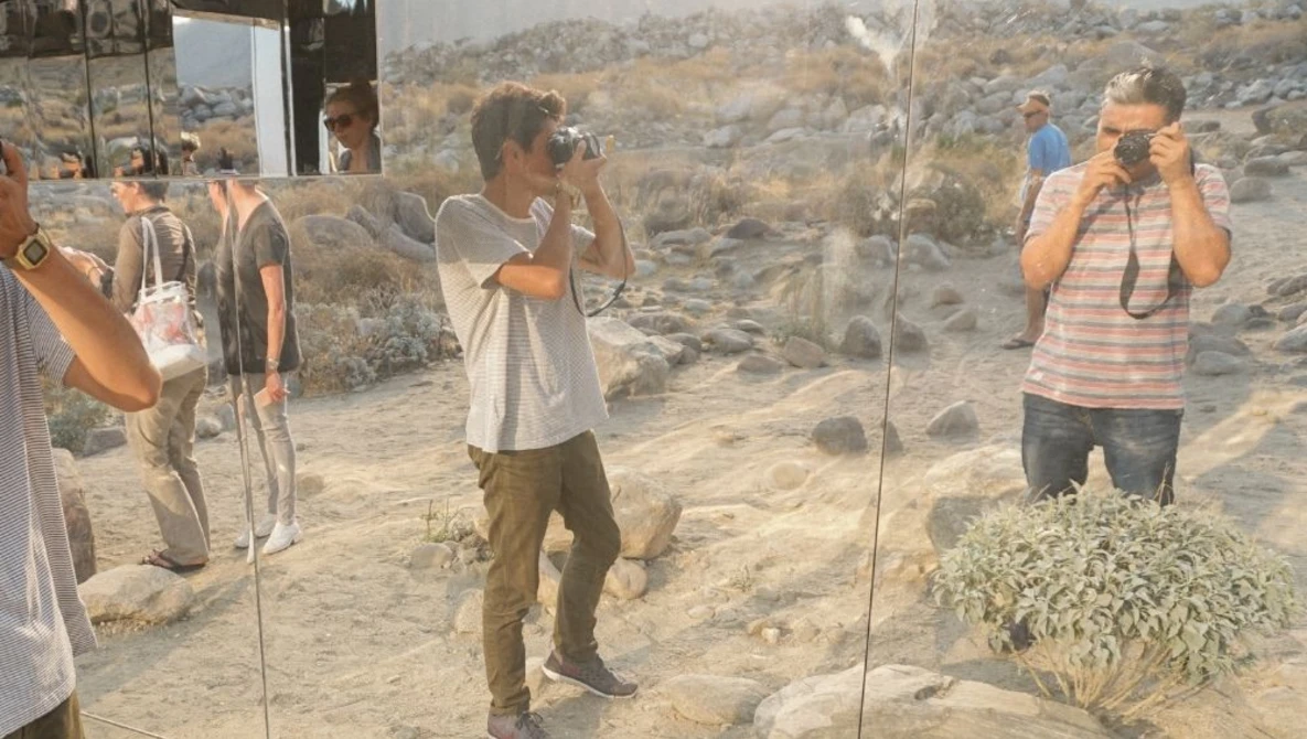 Photographers shooting in a desert landscape with rock formations visible through glass panels.