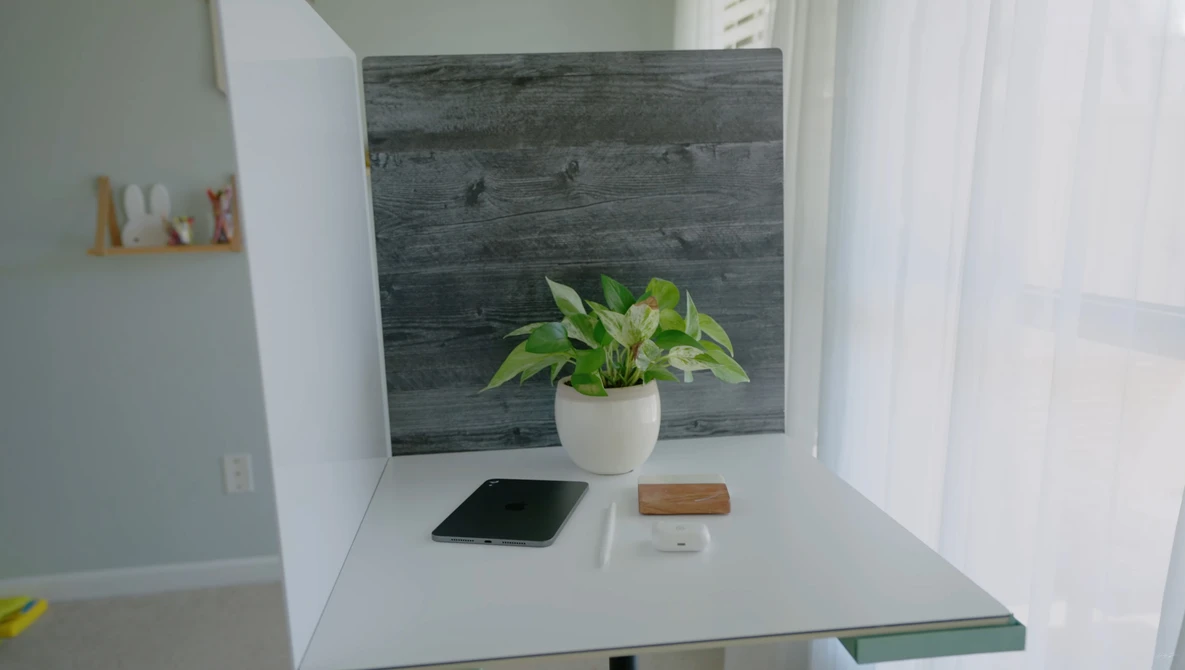 Minimalist desk setup with potted plant, smartphone, and wooden accessories against dark wood backdrop.