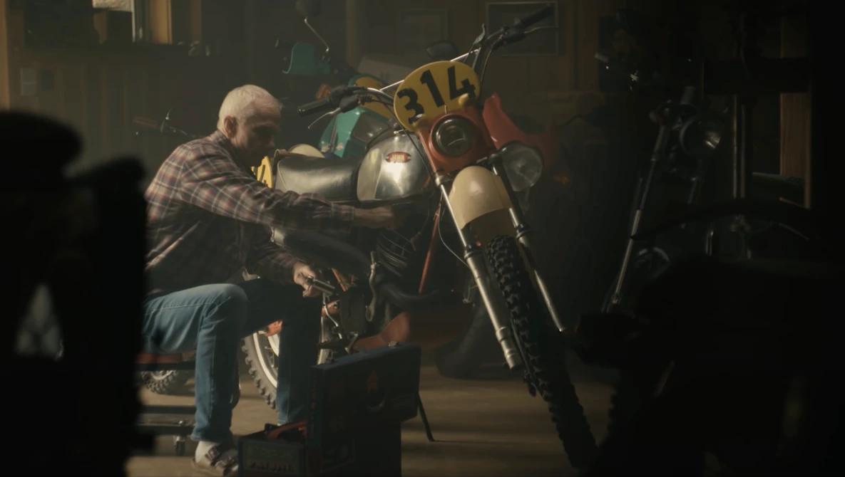 Older man working on a motorcycle in a dimly lit garage or workshop setting.