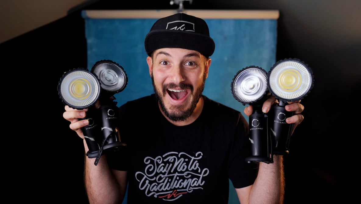 Enthusiastic man holding four LED panel lights in front of a blue backdrop.