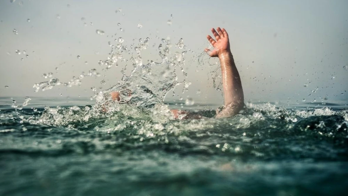 Person struggling in turbulent ocean water with one arm raised above the surface.