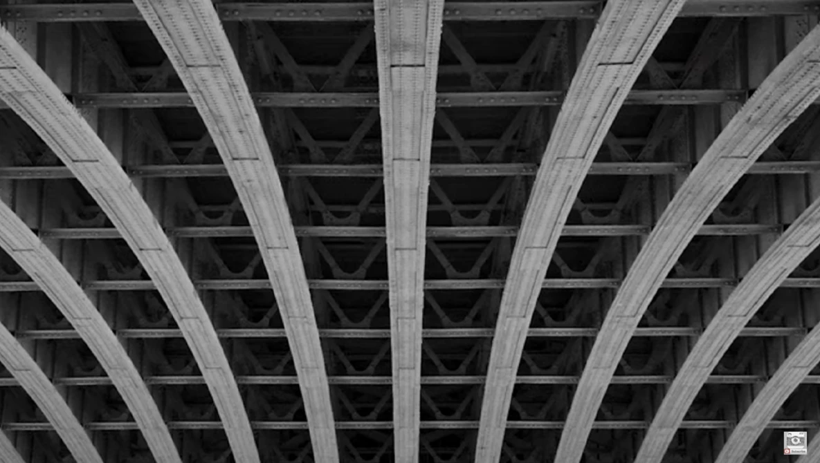 Concrete underpass with radiating ribbed support beams creating symmetrical geometric pattern in black and white.