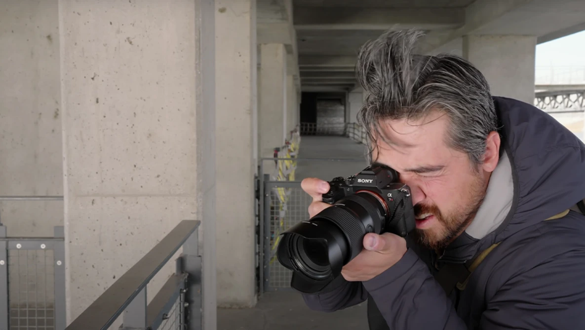 Photographer holding a DSLR camera with telephoto lens while composing a shot in an industrial concrete corridor.