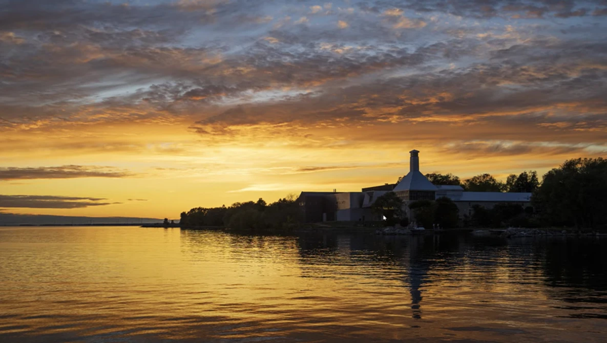 Silhouetted waterfront buildings reflected in calm water at golden hour sunset.