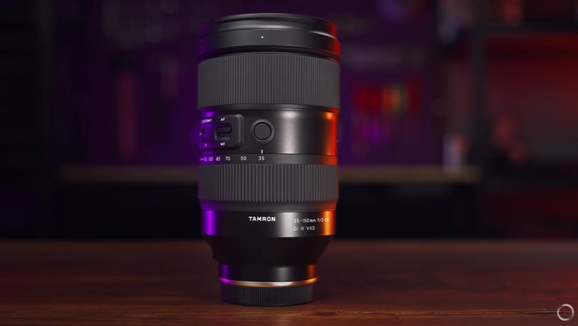 Tamron telephoto zoom lens displayed vertically on wooden surface with purple and orange accent lighting.