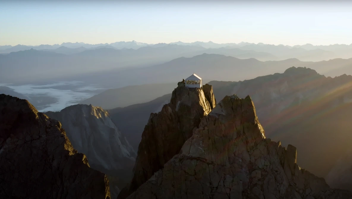 Mountain monastery perched on a rocky peak at sunrise, with layered mountain ranges and morning mist in the valley below.
