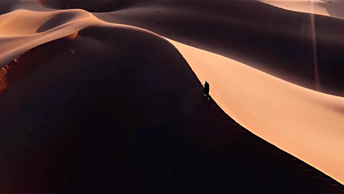 Silhouetted figure standing on a sand dune ridge during golden hour with dramatic shadow and warm desert light.