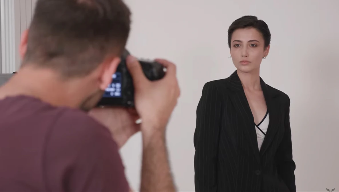 Photographer holding a camera on tripod photographing a woman in business attire during a studio portrait session.