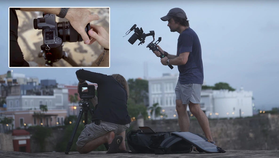 Two videographers operating gimbal stabilizers on a rooftop overlooking an urban skyline at dusk.