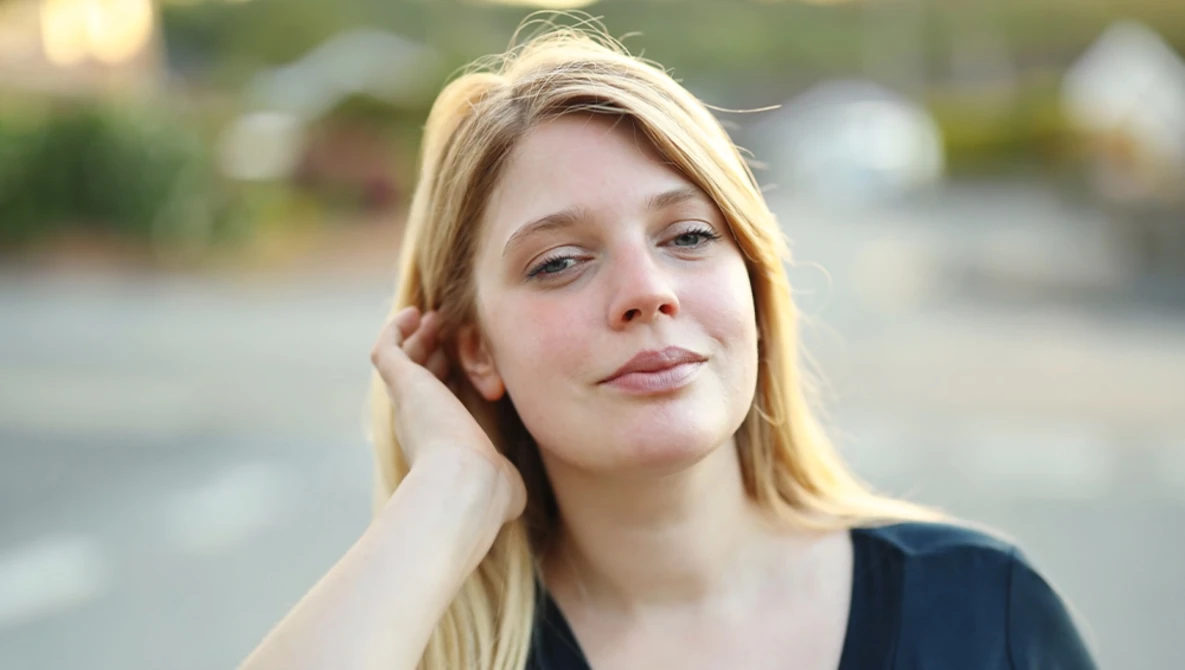 Young woman with blonde hair gazing downward in outdoor natural light.