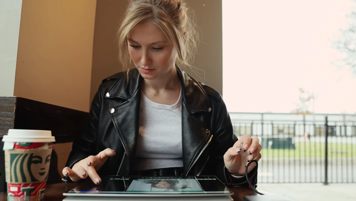 Woman with blonde hair wearing black leather jacket looking down at tablet device.