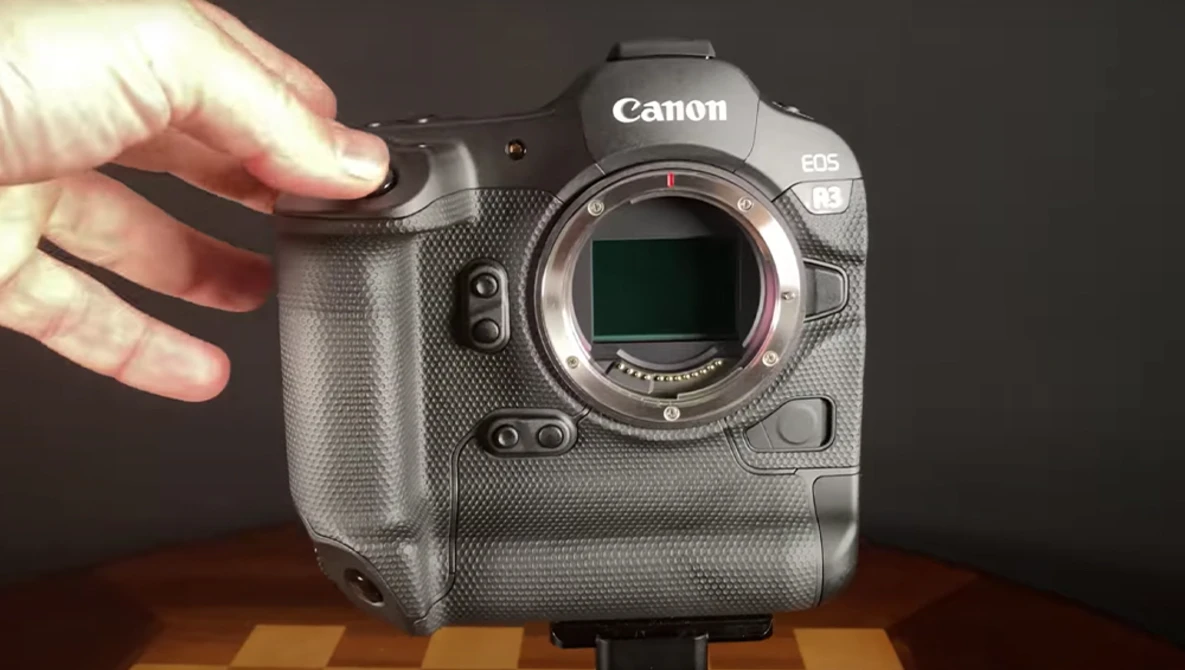 Canon EOS R5 mirrorless camera held in hand, showing open shutter and sensor against dark background.