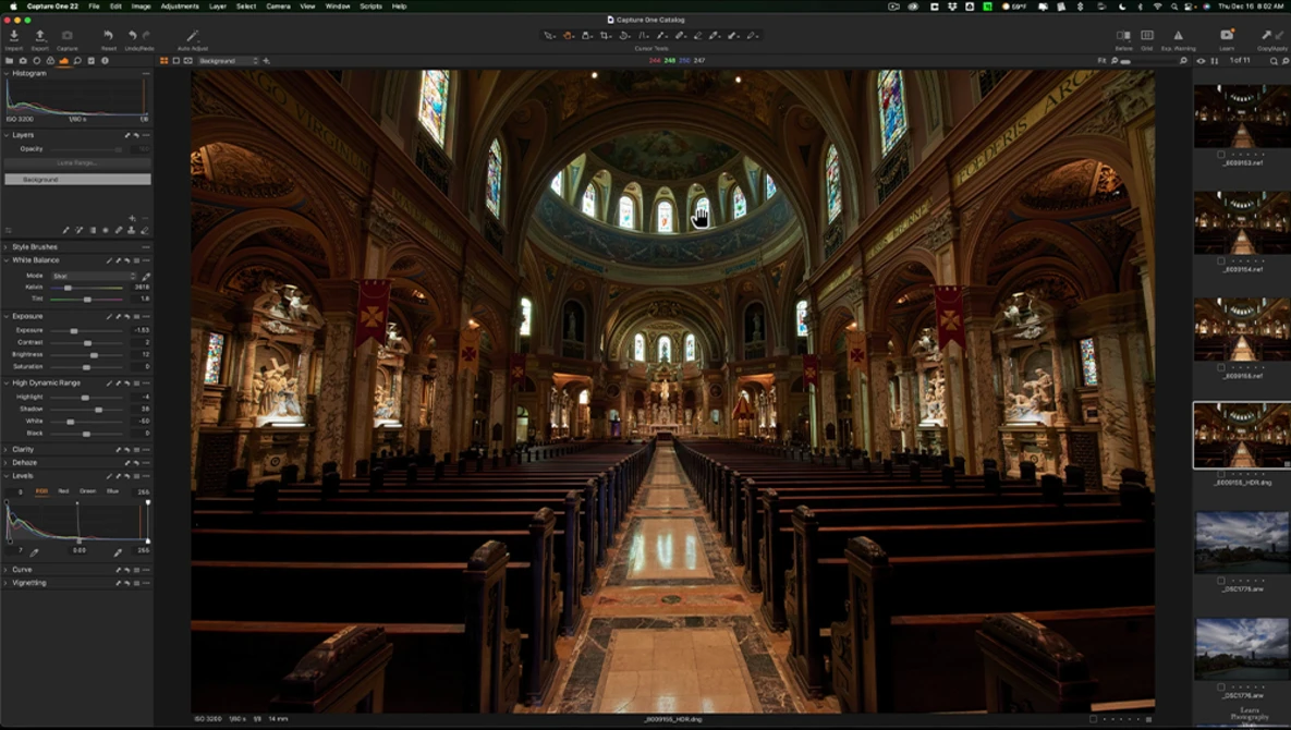 Interior of a grand cathedral with ornate wooden pews lining a central aisle, illuminated by stained glass windows and warm architectural lighting.