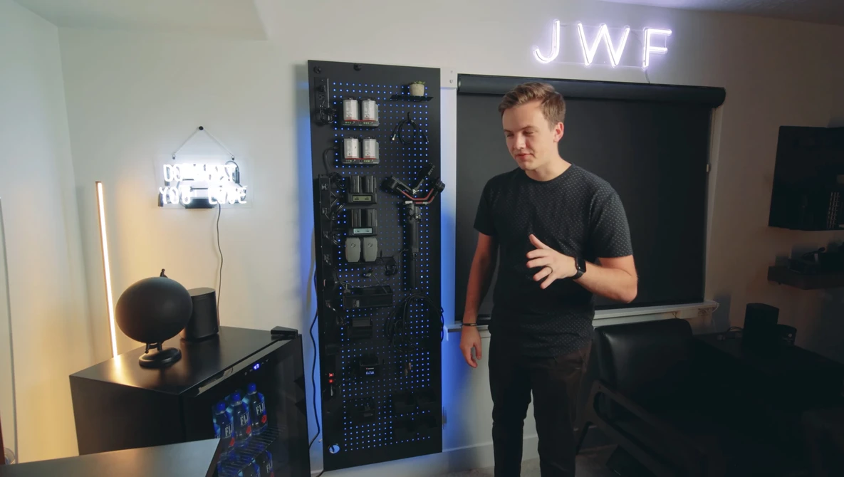 Man in black t-shirt gesturing while speaking next to server equipment and lighting setup in studio.