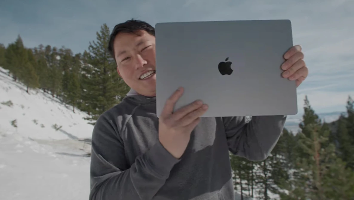 Person holding a large tablet device in front of their face outdoors in a snowy mountain landscape.