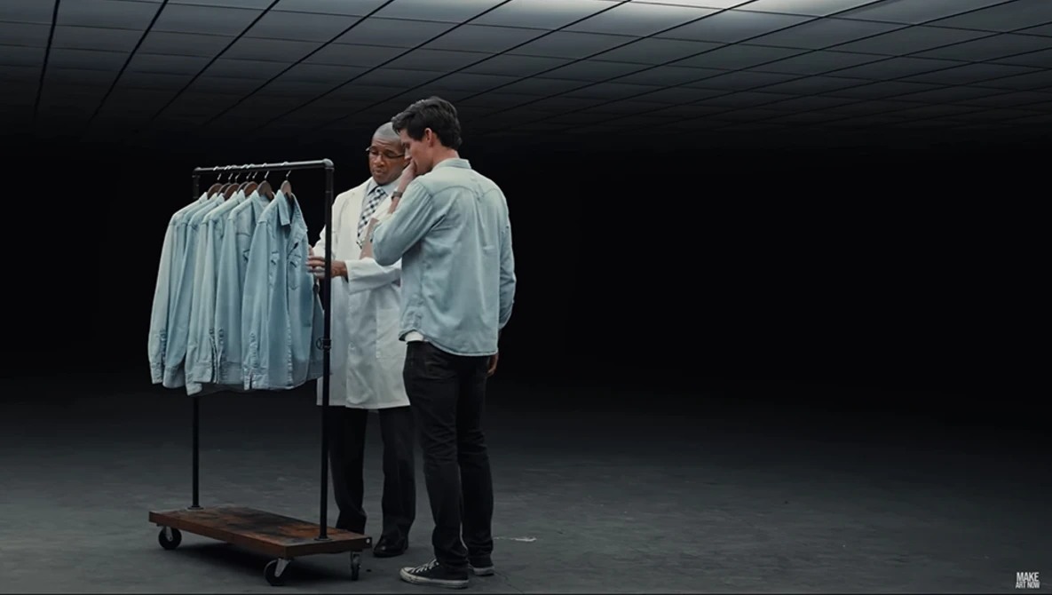 Two people examining garments on a rolling rack in a minimalist studio space with dark walls.