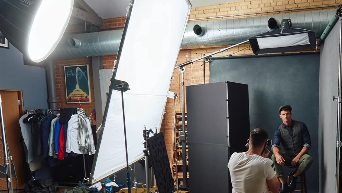 Professional photography studio setup with two people during a portrait shoot, featuring large softbox lighting and reflector panels.