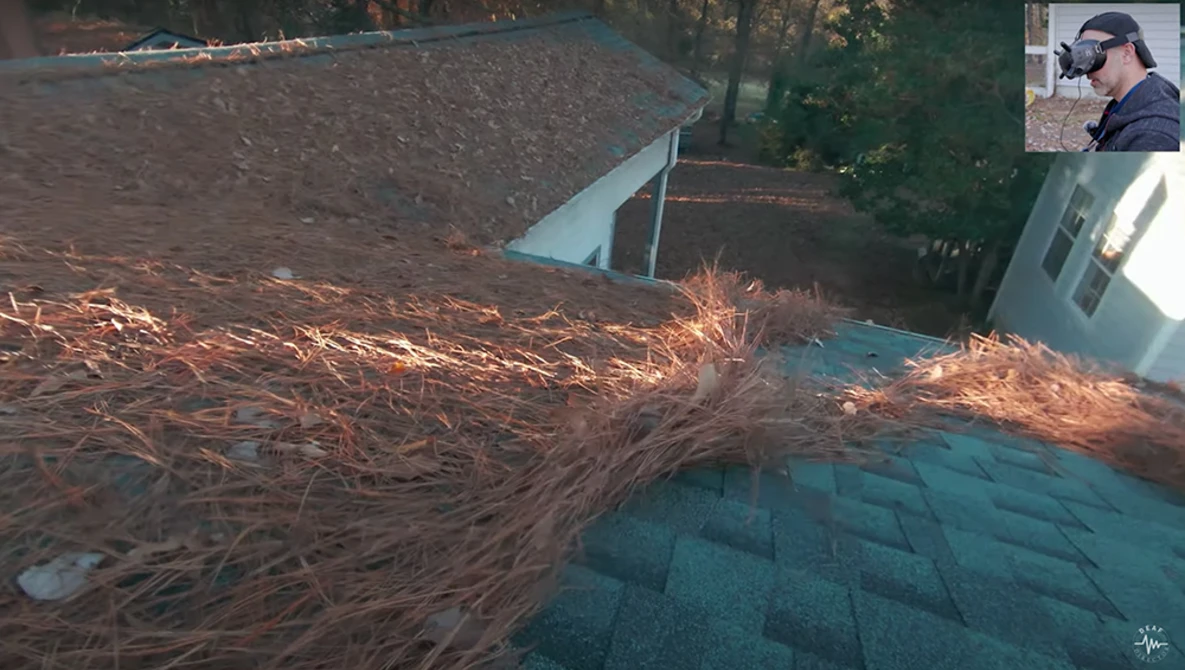 Roof covered with pine needles and debris next to a residential structure with shingle roofing.