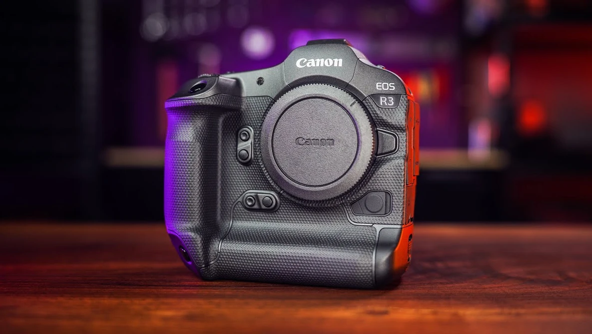 Canon EOS R3 mirrorless camera body displayed against a blurred bokeh background with purple and red ambient lighting.