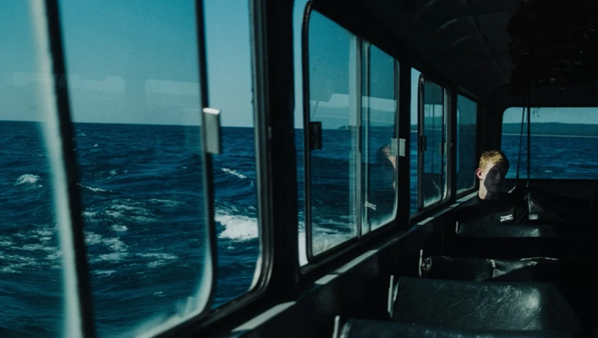 Person sitting inside a ferry cabin looking out at open ocean through large windows.