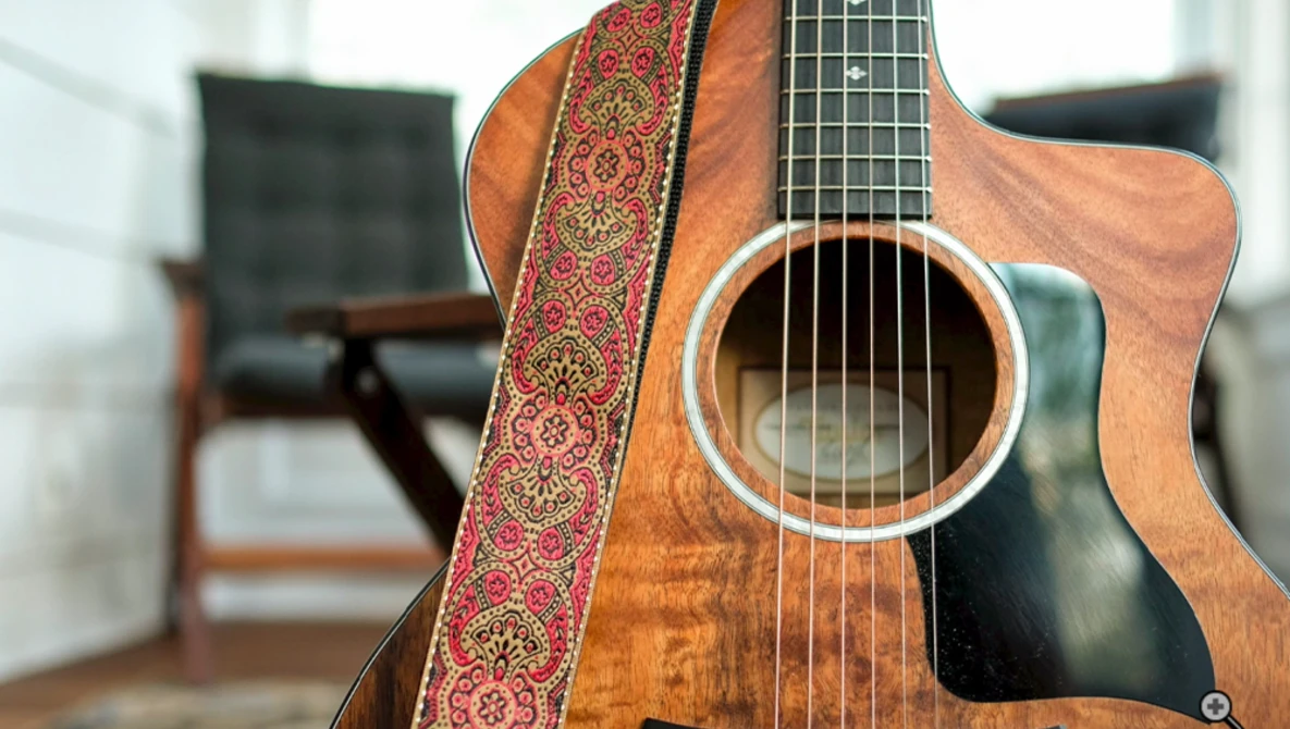 Acoustic guitar with decorative red and gold strap in an interior space with wooden furniture.