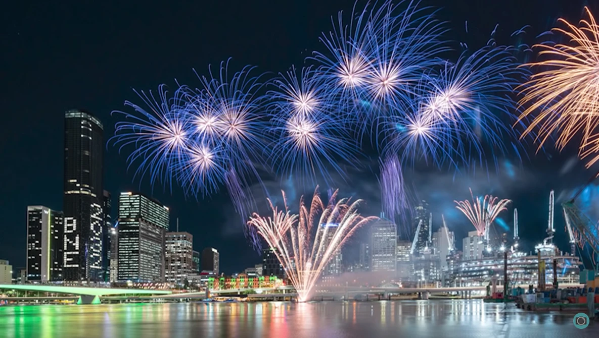 Fireworks exploding over a city skyline reflected in calm water at night.