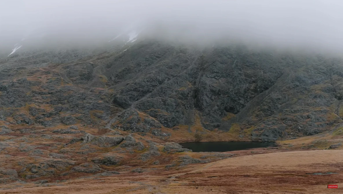 Misty mountain landscape with rocky peaks shrouded in fog and a small alpine lake nestled in the valley below.