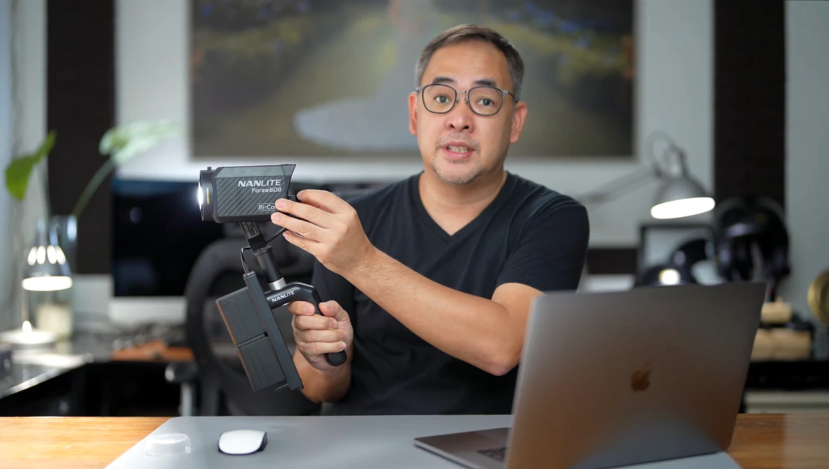 Content creator demonstrates a gimbal stabilizer while seated at a desk with laptop.