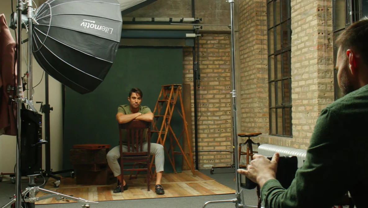 Photographer adjusting subject's posture during studio portrait session with professional lighting setup.
