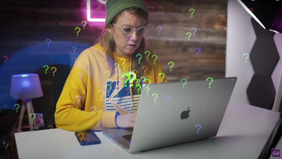 Person wearing yellow jacket and glasses at laptop surrounded by floating question mark graphics.