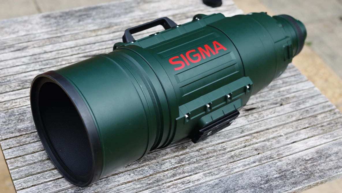 Sigma APO telephoto lens in forest green with red branding, displayed horizontally on weathered wood surface.