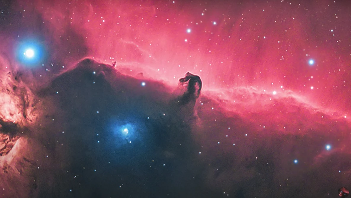 The Horsehead Nebula silhouetted against glowing pink hydrogen gas with bright blue stars scattered throughout the cosmic dust.