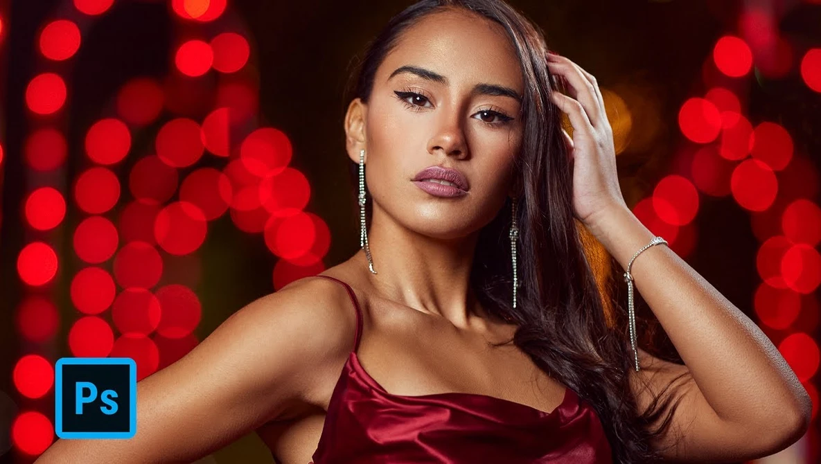 Woman in burgundy satin dress against red bokeh background with long dark hair and dangling earrings.
