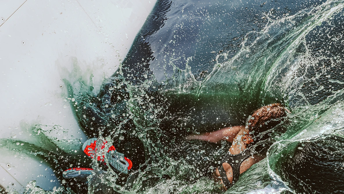 Overhead view of a person in water surrounded by splashing waves and green foliage.
